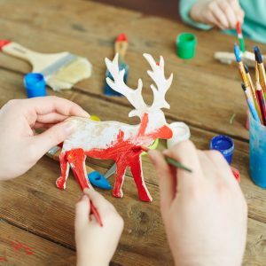 Hands of adult and kid painting wooden deer in red